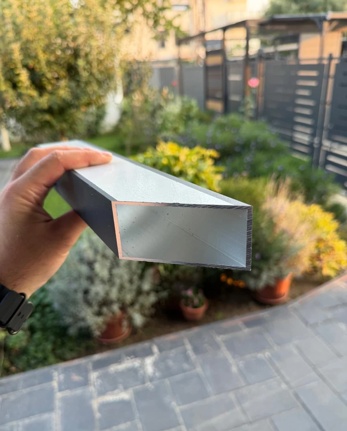 Ramă de poartă încropită din țeavă pătrată obișnuită, cu îmbinări și găuri de prindere rămase la vedere pe suprafața profilului de aluminiu.